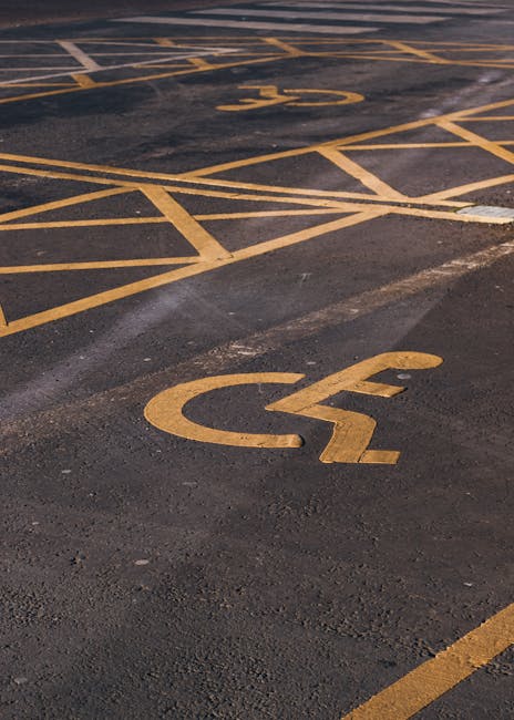 A close-up view of a parking lot surface showing multiple reserved parking spaces marked with yellow lines and wheelchair symbols painted on the dark asphalt. The image highlights the geometric arrangement of the lines and symbols, with some spaces positioned on the pavement, which appears freshly painted. This setting is outside a residential or commercial building, suggesting an area where vehicles, including removals vans used by Man with Van Preston, are arranged for loading or unloading furniture and packing materials during home relocation processes. The lighting indicates daytime conditions, with shadows cast by the markings, and the overall scene emphasizes organized parking for accessible and designated vehicle spaces, relevant to safe and efficient moving and transport operations associated with professional removals services.